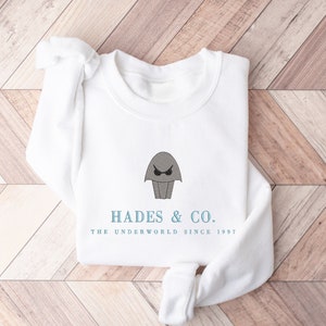 May include: White sweatshirt with a gray cartoon character wearing a crown and the text "Hades & Co. The Underworld Since 1997"