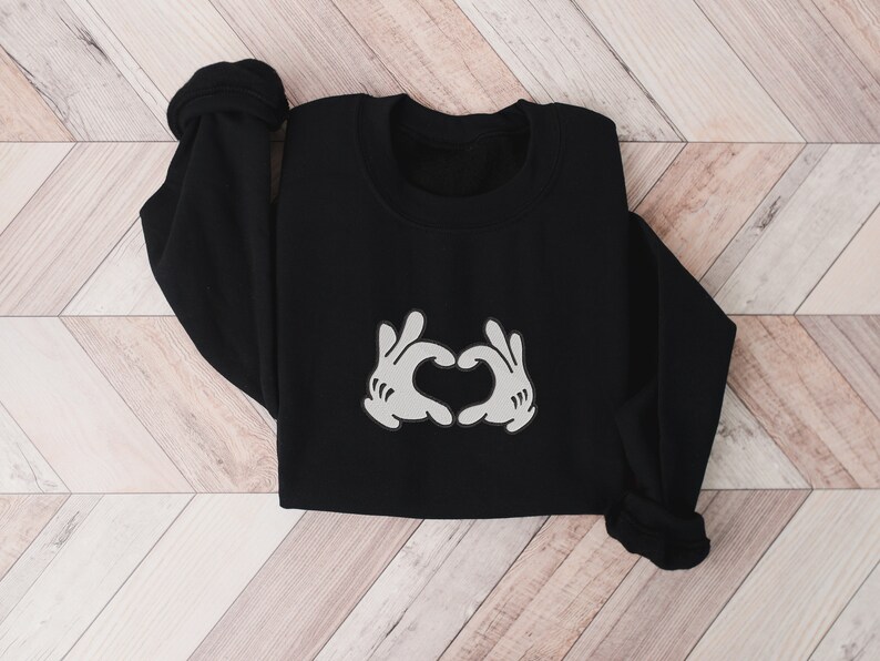 K&ouml;nnte beinhalten: Schwarzer Pullover mit einem wei&szlig;en Aufdruck von zwei H&auml;nden, die ein Herz bilden.