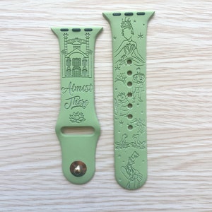 May include: A sage green silicone watch band featuring engraved illustrations of a building, a lotus flower, and the text "Almost There" on one side, with characters, a crown, and small stars engraved on the other side, including a metal pin closure.