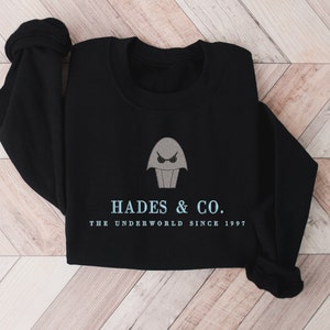 May include: Black sweatshirt with a gray embroidered image of a cartoon character with a single eye and the text "Hades & Co. The Underworld Since 1997."