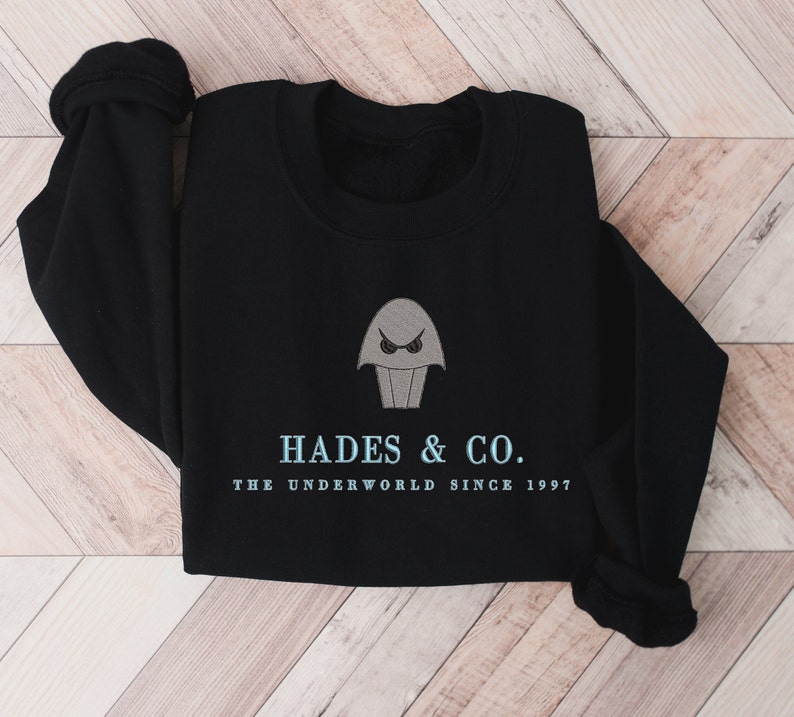 May include: Black sweatshirt with a gray embroidered image of a cartoon character with a single eye and the text "Hades & Co. The Underworld Since 1997."