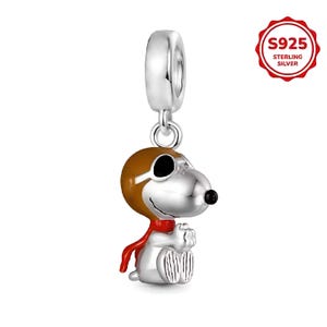 Può includere: Un charm in argento raffigurante un cane dei cartoni animati con testa marrone, occhi neri e sciarpa rossa. Il charm è realizzato in argento sterling e ha un anello nella parte superiore per il fissaggio a un braccialetto o una collana.