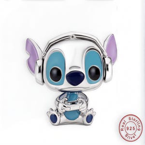 May include: A silver-colored figurine of the Disney character Stitch, wearing headphones and holding a game controller. The figurine has blue eyes, a blue nose, and purple ears. The base of the figurine is also blue.