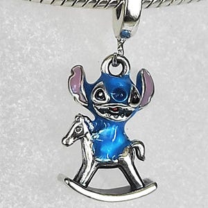 Pode incluir: Um berloque azul e prateado com um personagem de desenho animado em um cavalo de balan&ccedil;o. O berloque tem um corpo azul, orelhas rosa e uma base de cavalo de balan&ccedil;o prateada. O berloque &eacute; preso a uma pulseira de prata.