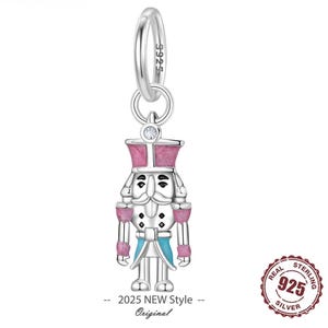 Peut inclure: Un charm en argent représentant un soldat casse-noisette, avec des détails roses et bleus. Le charm est conçu pour être attaché à un bracelet ou un collier. Le texte "2025 NEW Style - Original" est visible en bas.