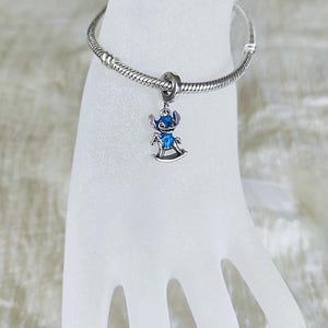 Pode incluir: Uma pulseira de berloques prateada com um berloque Stitch azul e prateado. O berloque apresenta Stitch num cavalo de baloi&ccedil;o. O berloque &eacute; detalhado com esmalte azul e detalhes prateados. A pulseira &eacute; feita de prata e tem um design de corrente de cobra.