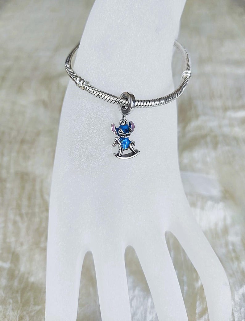 Pode incluir: Uma pulseira de berloques prateada com um berloque Stitch azul e prateado. O berloque apresenta Stitch num cavalo de baloi&ccedil;o. O berloque &eacute; detalhado com esmalte azul e detalhes prateados. A pulseira &eacute; feita de prata e tem um design de corrente de cobra.