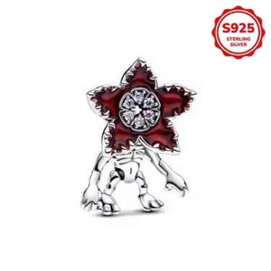 May include: A sterling silver charm featuring a Demogorgon design. The charm has a red flower-like head with a cluster of clear stones at the center. The body is silver with detailed features, and the charm is stamped with "S925 STERLING SILVER".