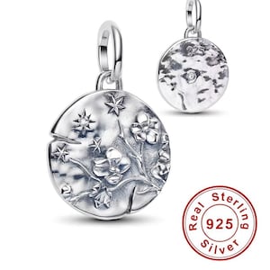 Op de afbeelding: Een zilveren bedel met een bloemen- en sterrenontwerp. De voorkant heeft een gedetailleerd reliëf van bloemen en sterren, terwijl de achterkant een textuuroppervlak heeft. De hanger is rond met een lus om aan te bevestigen.