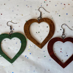 Peut inclure: Trois paires de boucles d'oreilles en forme de cœur en cuir. Les boucles d'oreilles sont en vert, marron et rouge. Les boucles d'oreilles sont suspendues à des crochets argentés.