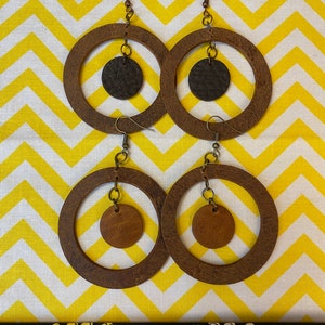 May include: A pair of brown wooden hoop earrings with a smaller brown leather circle hanging from each hoop.