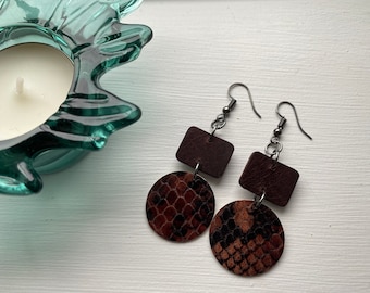 Peut inclure: Une paire de boucles d'oreilles pendantes avec des carrés en cuir marron et des pièces rondes en cuir marron avec un motif peau de serpent.