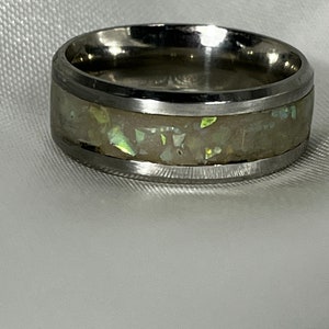 May include: A silver band with a white opal inlay. The band is polished and has a smooth finish.