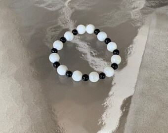 May include: A black and white beaded bracelet with alternating round beads. The bracelet is made of natural materials and has a simple, elegant design.