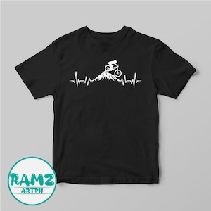 May include: Black t-shirt with a white graphic of a mountain biker riding up a mountain with a heartbeat line. The graphic is centered on the shirt.