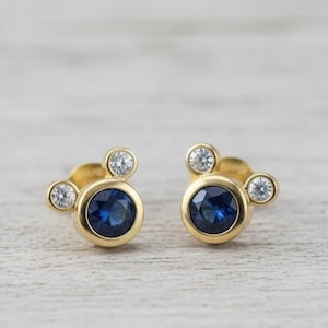 Elegant cubic zirconia stud earrings with gold plating – designed with a deep blue stone center and sparkling side crystals.
 blue CZ earrings, gold plated, elegant jewelry, crystal studs, dainty earrings