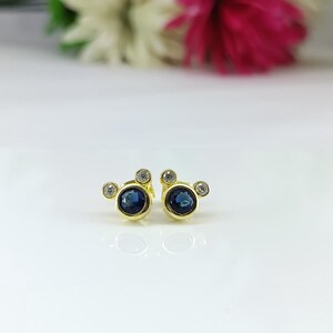Mickey Mouse shaped gold earrings with cubic zirconia on white background – ideal birthday or Christmas gift for girls or women
Petite gold plated earrings with round blue cubic zirconia center and twin white CZ sparkle. Perfect dainty gift jewelry.
 petite earrings, blue CZ studs, dainty jewelry, gold earrings, minimal gift