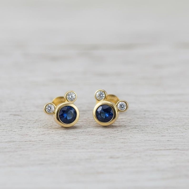 Elegant cubic zirconia stud earrings with gold plating – designed with a deep blue stone center and sparkling side crystals.
 blue CZ earrings, gold plated, elegant jewelry, crystal studs, dainty earrings