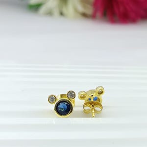 Close-up of Disney-inspired blue CZ mouse earrings in 18K gold plating – elegant design, great gift for sister or daughter
Luxury minimal earrings featuring blue CZ center stone and small crystal accents. Chic gold plated studs by JewelsMinimal.
luxury earrings, blue CZ jewelry, minimal studs, gold plated earrings, chic design