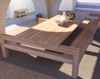 May include: A large wooden table with two benches attached to either side. The table is made of natural wood and has a rustic look. The benches are also made of wood and have a simple design.