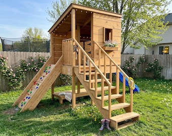 Könnte beinhalten: Ein Holzspielhaus mit Rutsche, Kletterwand und Treppe. Das Spielhaus hat einen kleinen Blumenkasten mit Blumen und eine blaue Rutsche. Die Kletterwand hat farbige Klettergriffe. Das Spielhaus steht in einem grasbewachsenen Garten.