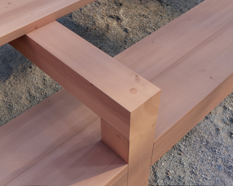 May include: Close-up of a wooden bench with a natural reddish-brown finish. The bench is made of thick planks of wood and has a simple, rectangular design. The wood is joined together with a metal screw.
