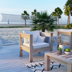 Puede incluir: Dos sillas de madera con cojines blancos y una mesa de caf&eacute; de madera a juego en una terraza de madera blanca con una playa de arena blanca y palmeras en el fondo.