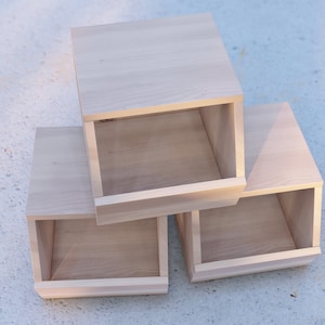 May include: Three wooden boxes stacked on top of each other. The boxes are all the same size and shape, and they have a light wood finish. The boxes are open on the front, revealing the empty space inside.