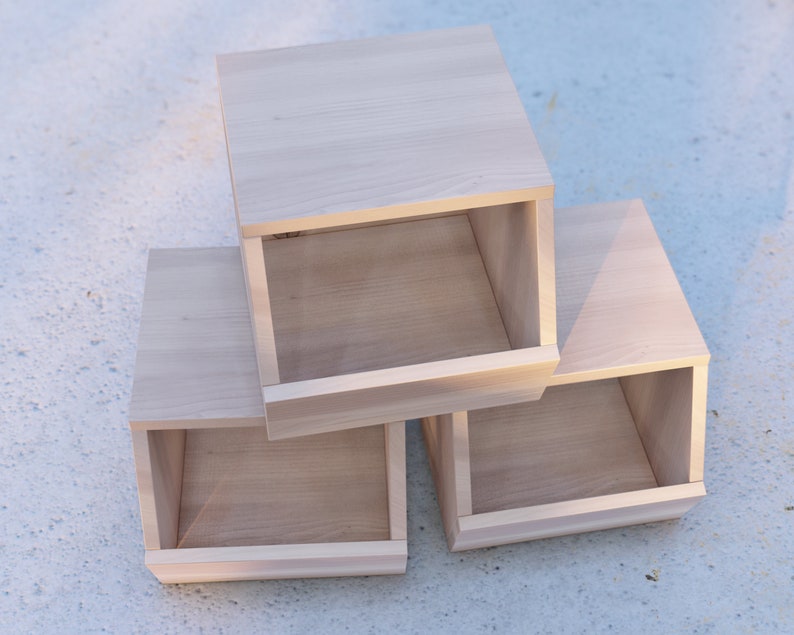 May include: Three wooden boxes stacked on top of each other. The boxes are all the same size and shape, and they have a light wood finish. The boxes are open on the front, revealing the empty space inside.