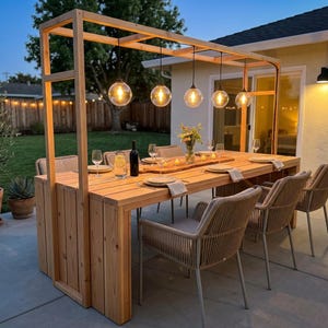 Puede incluir: Juego de comedor al aire libre con mesa y sillas de madera. La mesa es de madera clara y tiene una zona de bar integrada. Seis sillas con respaldos tejidos rodean la mesa. Encima, cinco luces de globo cuelgan de un marco de madera.