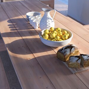 K&ouml;nnte beinhalten: Ein Holztisch mit einem wei&szlig;en Krug, einer Sch&uuml;ssel mit gelben &Auml;pfeln und zwei Broten auf einem Holzbrett.