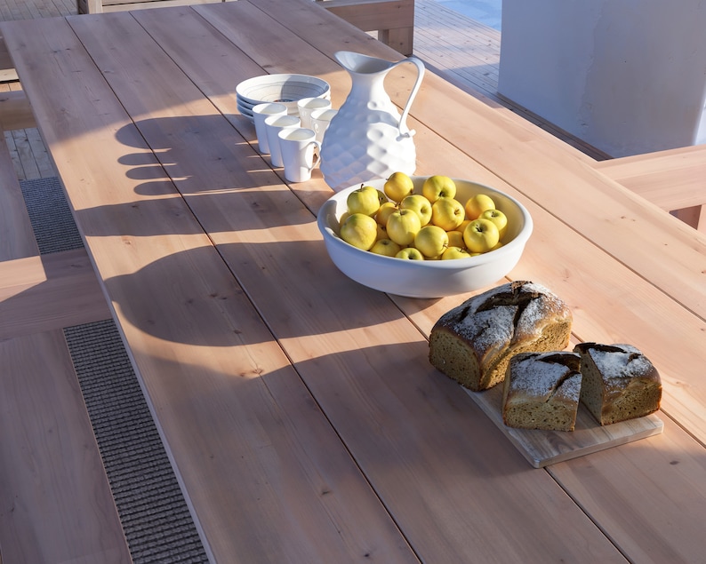 K&ouml;nnte beinhalten: Ein Holztisch mit einem wei&szlig;en Krug, einer Sch&uuml;ssel mit gelben &Auml;pfeln und zwei Broten auf einem Holzbrett.