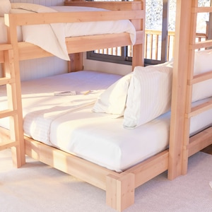 May include: A wooden bunk bed with a white mattress and white bedding on the top bunk. The bottom bunk has a white mattress and white bedding with a pillow on the bed. The bed is made of natural wood and has a ladder on the side.