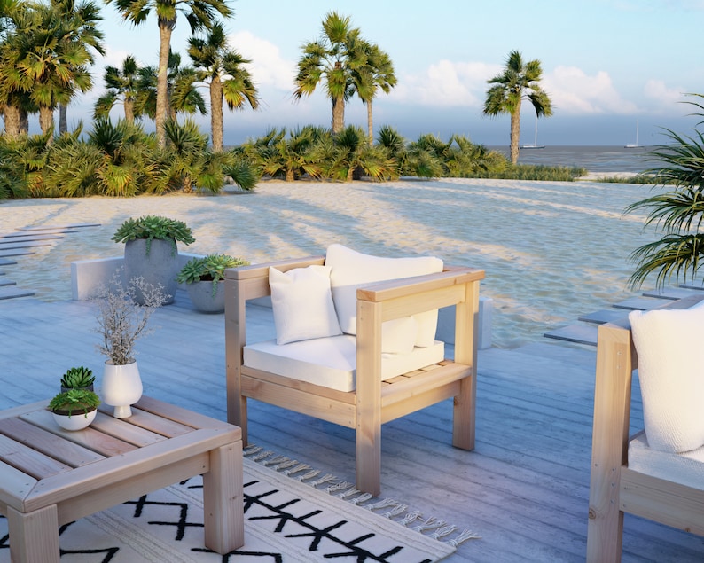 Puede incluir: Dos sillas de madera con cojines blancos y una mesa de caf&eacute; de madera en una terraza de madera con una playa y palmeras en el fondo.
