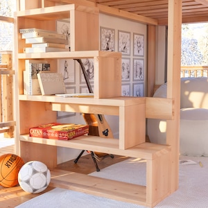 Puede incluir: Una estanter&iacute;a de madera con varios estantes, algunos de los cuales est&aacute;n abiertos y otros cerrados. Los estantes est&aacute;n llenos de libros, juegos y otros art&iacute;culos. Hay una guitarra apoyada en la estanter&iacute;a. La estanter&iacute;a est&aacute; en una habitaci&oacute;n con una pared blanca y una ventana grande. Hay un puf blanco en la habitaci&oacute;n.