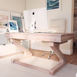 Puede incluir: Un escritorio de madera clara con una base en forma de Z y un monitor de computadora blanco en la parte superior. El escritorio est&aacute; en una oficina en casa con una alfombra blanca y pisos de madera.