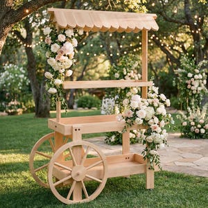 May include: A wooden cart with a scalloped roof, shelves, and large spoked wheels. The cart is decorated with white and pink flowers. The scene is set outdoors with trees and fairy lights in the background.