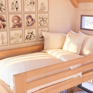 Puede incluir: Una cama individual blanca con un marco de madera y ropa de cama blanca. La cama est&aacute; en una habitaci&oacute;n con una ventana y una pared decorada con dibujos de personajes de anime enmarcados.
