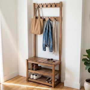May include: A wooden entryway organizer with a bench, shoe storage, and coat rack. A tan tote bag, denim jacket, and scarf hang from the hooks. Shoes and sunglasses are on the bench. The wood has a warm, natural finish.