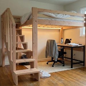 May include: A wooden loft bed with a built-in staircase and a desk underneath. The bed frame and staircase are made of light-colored wood. A desk with a black frame and a laptop is positioned under the bed. A rug and a chair are also present.