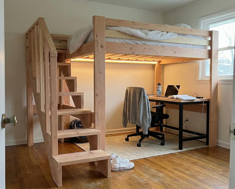 May include: A wooden loft bed with a built-in staircase and a desk underneath. The bed frame and staircase are made of light-colored wood. A desk with a black frame and a laptop is positioned under the bed. A rug and a chair are also present.