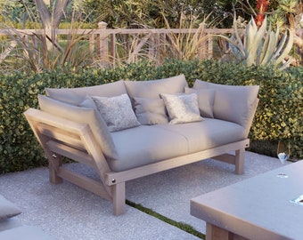 May include: A light gray outdoor lounge chair with a wooden frame and a cushioned seat and back. The chair is positioned on a patio with a stone floor and green plants in the background.