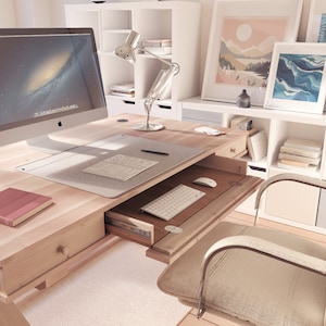 Puede incluir: Un escritorio de madera clara con un caj&oacute;n que se desliza para revelar un teclado y un rat&oacute;n. El escritorio tiene un monitor de computadora blanco, una l&aacute;mpara y un libro en la parte superior. Hay una silla blanca en primer plano.