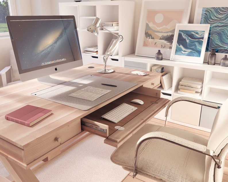 Puede incluir: Un escritorio de madera clara con un caj&oacute;n que se desliza para revelar un teclado y un rat&oacute;n. El escritorio tiene un monitor de computadora blanco, una l&aacute;mpara y un libro en la parte superior. Hay una silla blanca en primer plano.