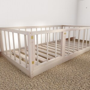 May include: A white wooden crib with a slatted design and a hinged door. The crib is on a beige carpet.
