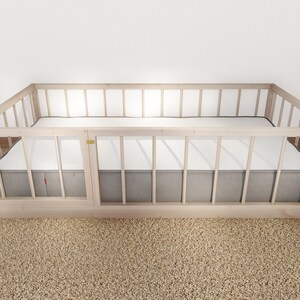 May include: A wooden crib with a gray mattress and a white sheet. The crib has a wooden frame with slats and a removable side panel.