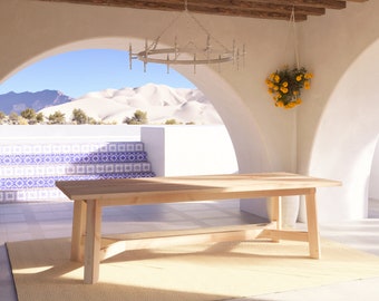 May include: A light wood dining table with a simple design, set on a beige rug in a white patio with a view of sand dunes through arched doorways. A white chandelier hangs from the ceiling and a hanging planter with yellow flowers is visible in the corner.
