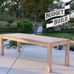 May include: A light wood rectangular table with four legs. The table is in a garden setting with green grass and plants in the background. The text "BUDGET BUILD UNDER $100" is visible in a banner above the table.