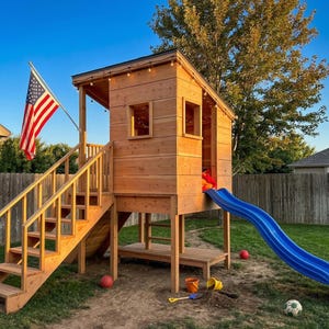Puede incluir: Una casa de juegos de madera con un tobogán azul, escaleras y una bandera estadounidense. La casa de juegos tiene una pequeña terraza y ventanas. El tobogán está unido al costado. Hay juguetes y un balón de fútbol en el suelo.