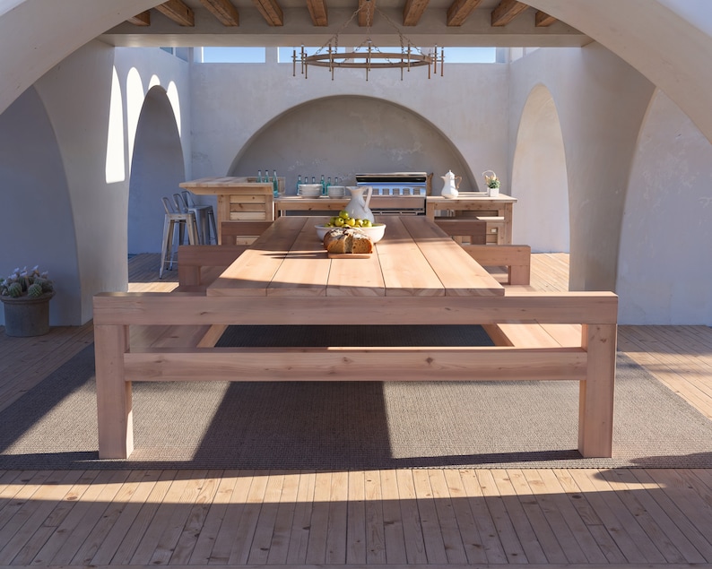 K&ouml;nnte beinhalten: Ein gro&szlig;er Esstisch aus Holz mit zwei B&auml;nken, auf einem braunen Teppich in einem wei&szlig;en, gew&ouml;lbten Patio. Der Tisch ist aus Naturholz gefertigt und hat einen rustikalen Look.